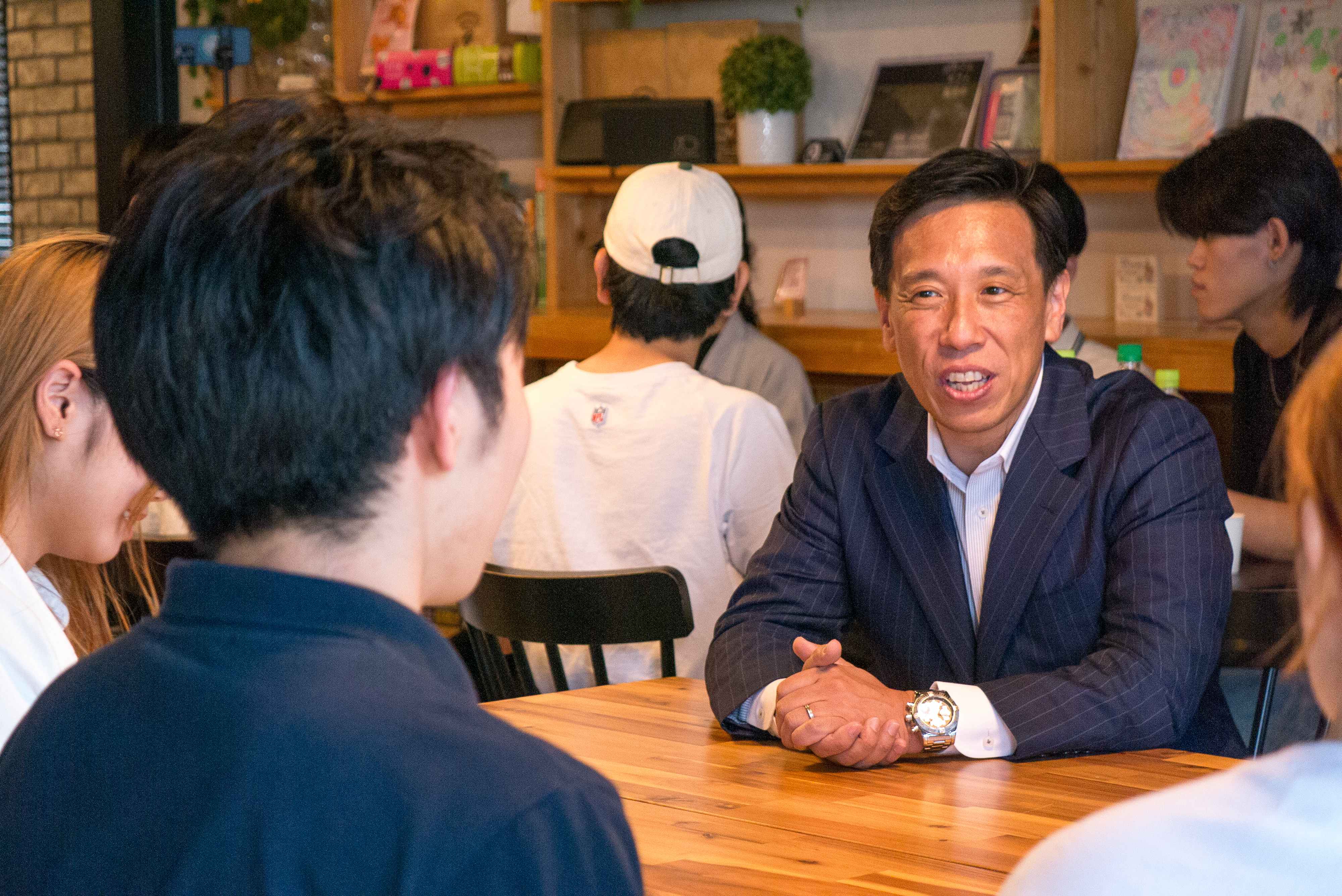 カフェのテーブルで学生と語り合う経営者